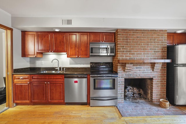 kitchen featuring dark stone counters, sink, ornamental molding, light wood-type flooring, and appliances with stainless steel finishes