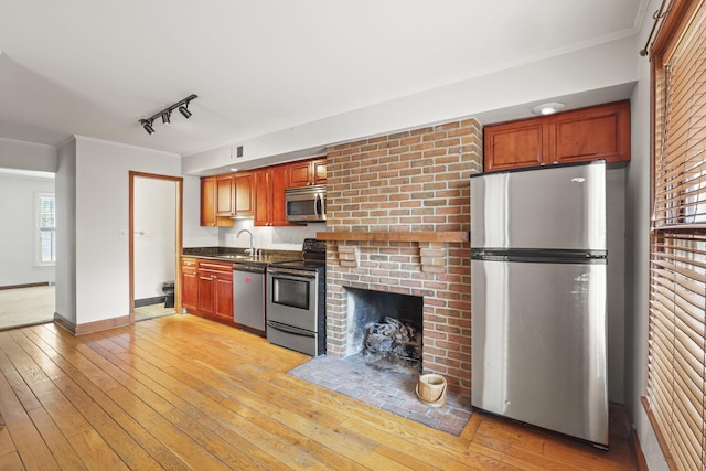 kitchen featuring appliances with stainless steel finishes, rail lighting, ornamental molding, sink, and light hardwood / wood-style flooring