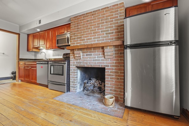 kitchen featuring light wood-type flooring, ornamental molding, appliances with stainless steel finishes, and a brick fireplace