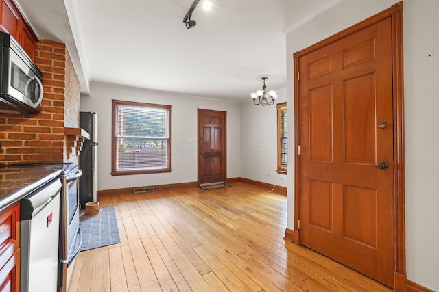 kitchen featuring appliances with stainless steel finishes, light wood-type flooring, ornamental molding, decorative light fixtures, and a chandelier