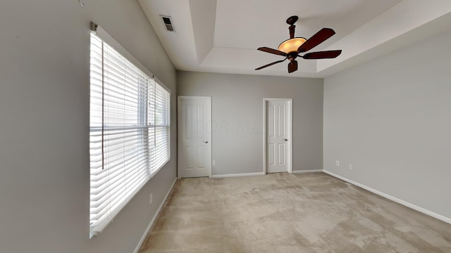 unfurnished bedroom with ceiling fan, light carpet, a tray ceiling, and multiple windows