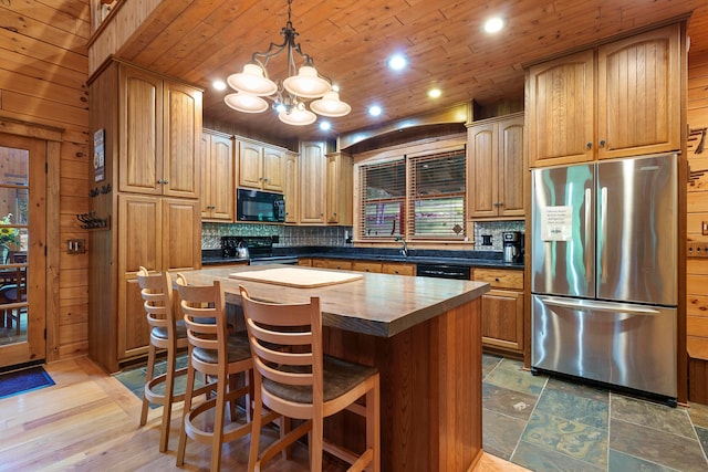 kitchen featuring black appliances, a kitchen island, wooden walls, and tasteful backsplash