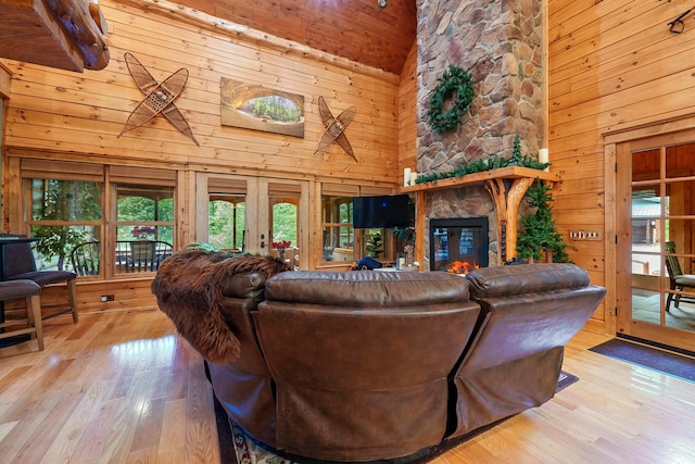 living room with wood walls, high vaulted ceiling, french doors, a fireplace, and light hardwood / wood-style floors