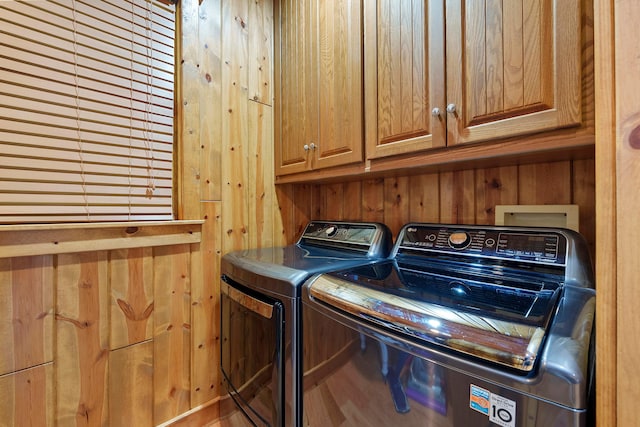 clothes washing area with washing machine and dryer, wooden walls, and cabinets