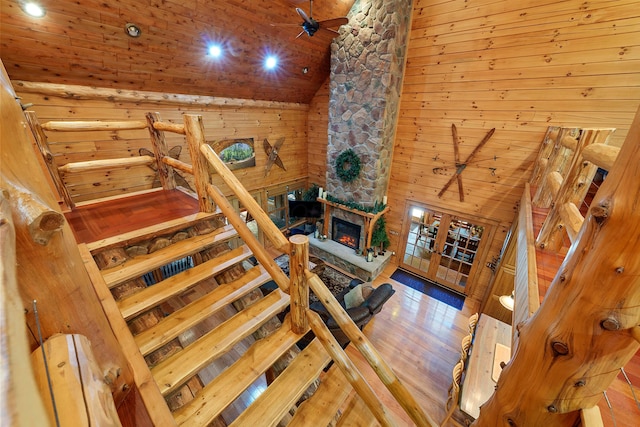 stairs with hardwood / wood-style floors, wood walls, high vaulted ceiling, ceiling fan, and a fireplace