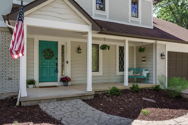 doorway to property with a garage, a shingled roof, a porch, and brick siding