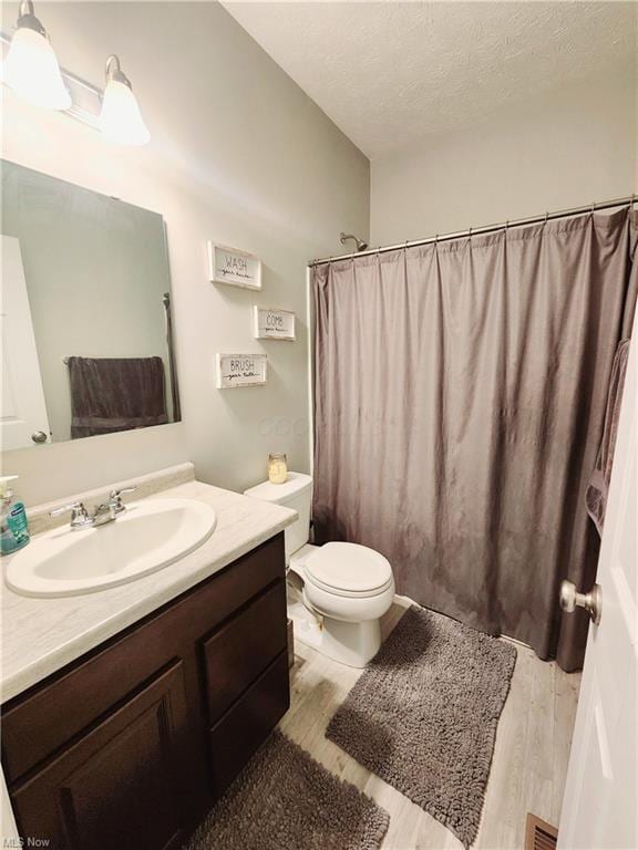 bathroom with curtained shower, hardwood / wood-style flooring, vanity, toilet, and a textured ceiling