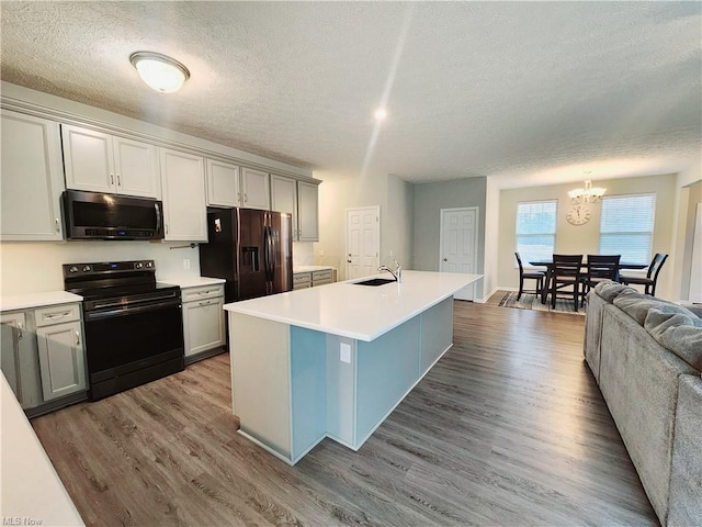 kitchen featuring sink, appliances with stainless steel finishes, gray cabinetry, wood-type flooring, and a center island with sink