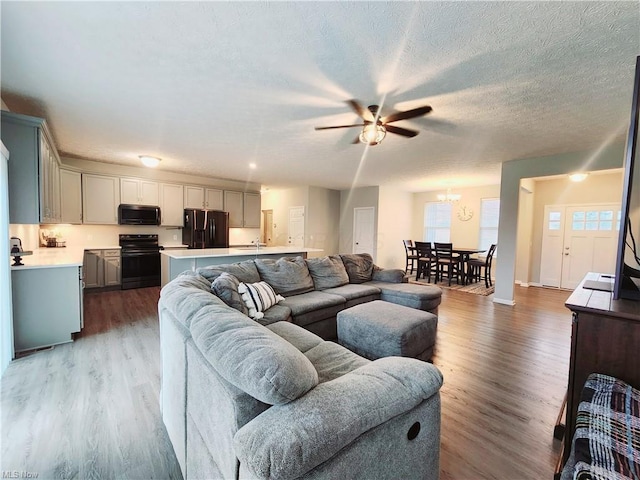 living room featuring ceiling fan, wood-type flooring, sink, and a textured ceiling