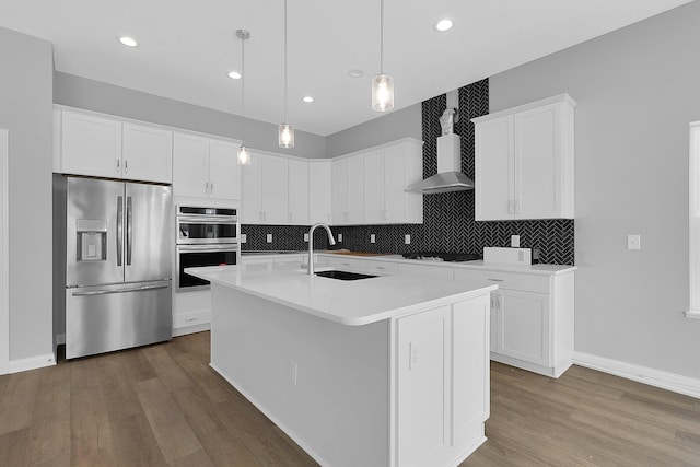 kitchen featuring a center island with sink, white cabinets, sink, appliances with stainless steel finishes, and decorative light fixtures