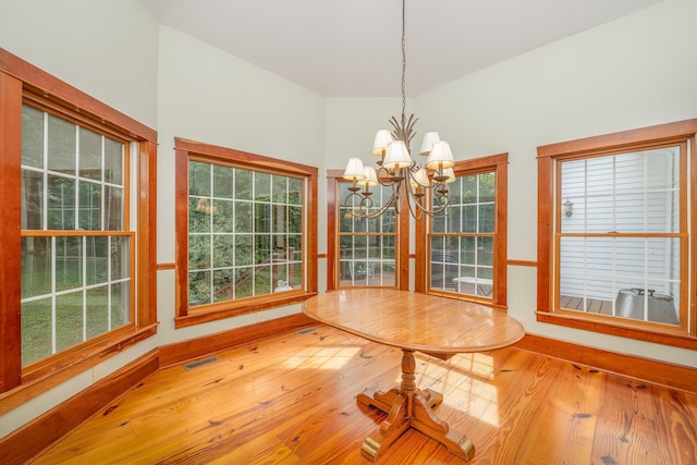 unfurnished dining area featuring hardwood / wood-style floors, vaulted ceiling, plenty of natural light, and a notable chandelier