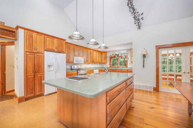 kitchen featuring lofted ceiling, white appliances, a center island with sink, hanging light fixtures, and light wood-type flooring