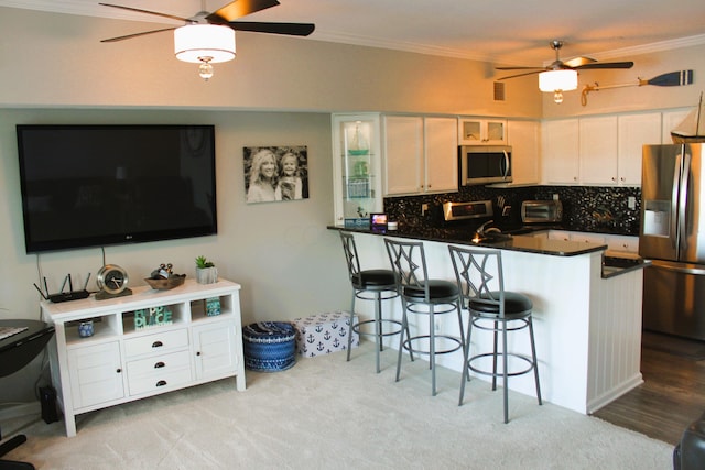 kitchen featuring a breakfast bar area, ornamental molding, white cabinetry, kitchen peninsula, and stainless steel appliances