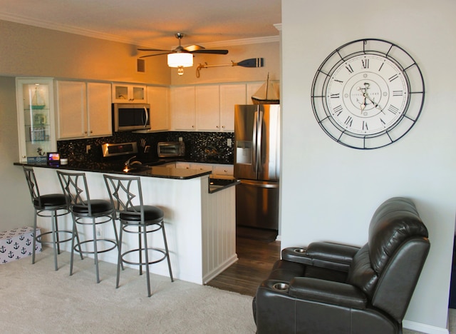 kitchen with kitchen peninsula, appliances with stainless steel finishes, dark hardwood / wood-style flooring, decorative backsplash, and crown molding