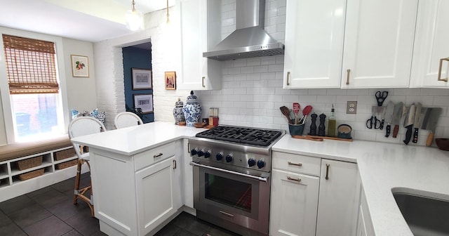 kitchen with white cabinets, wall chimney exhaust hood, high end stove, and kitchen peninsula