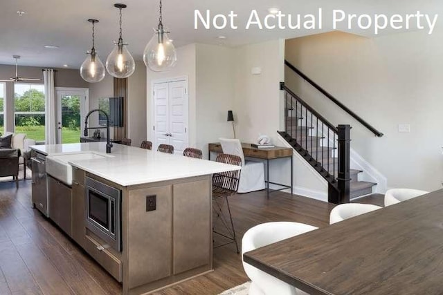 kitchen with dark wood-type flooring, a breakfast bar, stainless steel microwave, and an island with sink