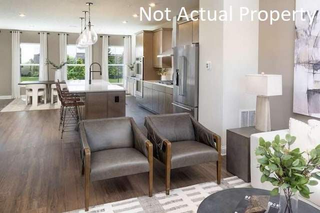 interior space with a kitchen island with sink, under cabinet range hood, dark wood-style flooring, light countertops, and appliances with stainless steel finishes