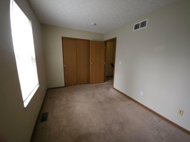 unfurnished bedroom featuring a textured ceiling, light colored carpet, and a closet