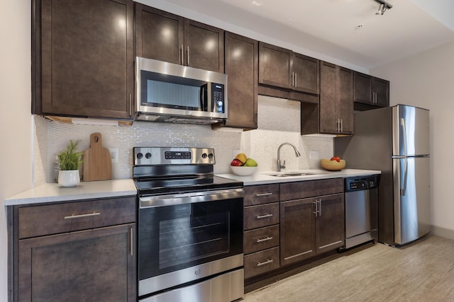 kitchen with dark brown cabinetry, sink, backsplash, appliances with stainless steel finishes, and light wood-type flooring