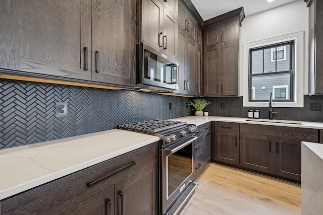 kitchen with dark brown cabinetry, tasteful backsplash, appliances with stainless steel finishes, light wood-style floors, and a sink