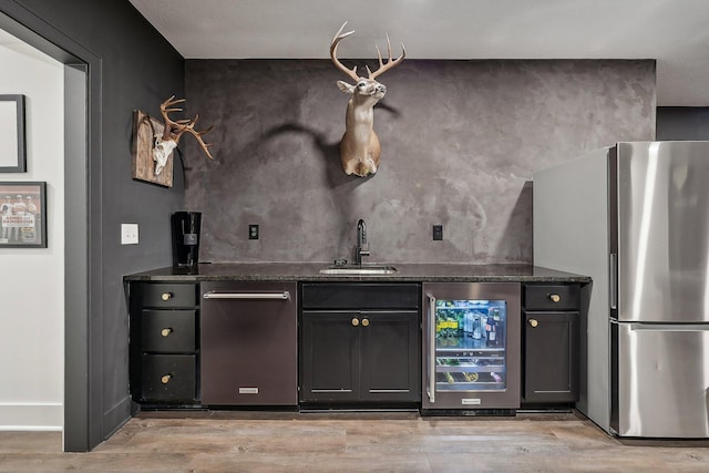 bar featuring wine cooler, indoor wet bar, freestanding refrigerator, a sink, and light wood-type flooring