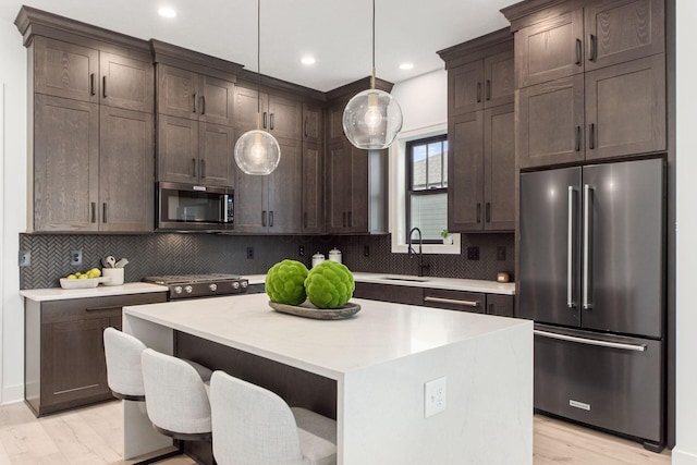 kitchen with premium appliances, a center island, decorative light fixtures, light countertops, and a sink