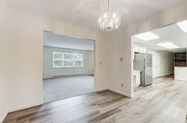 unfurnished dining area with light hardwood / wood-style floors, a baseboard heating unit, and an inviting chandelier