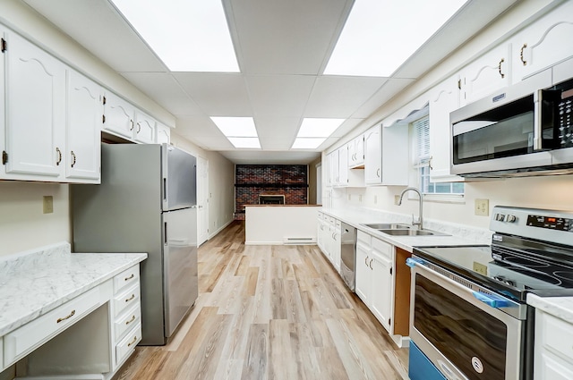 kitchen featuring white cabinets, sink, a brick fireplace, appliances with stainless steel finishes, and light hardwood / wood-style floors