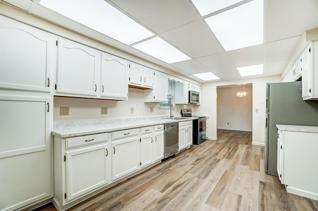 kitchen with a drop ceiling, white cabinets, stainless steel appliances, and light hardwood / wood-style floors