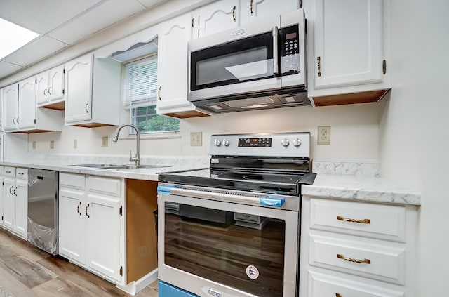 kitchen with appliances with stainless steel finishes, light wood-type flooring, a paneled ceiling, sink, and white cabinets