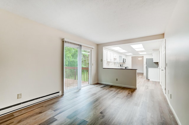 unfurnished living room featuring baseboard heating, light hardwood / wood-style floors, and a textured ceiling