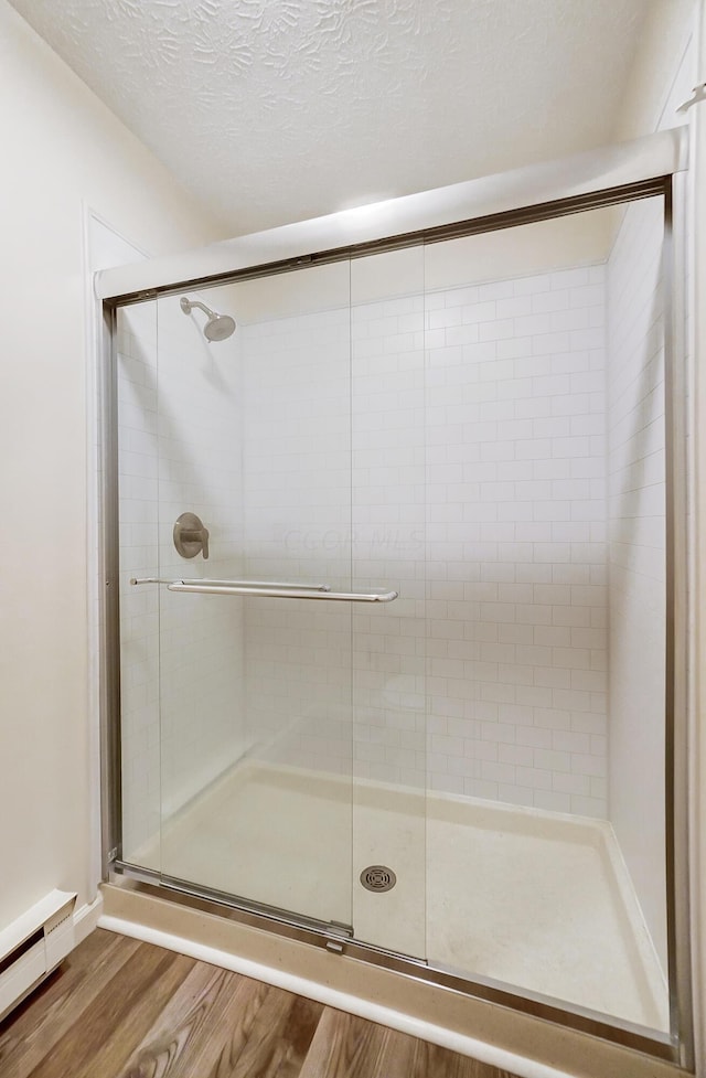 bathroom featuring hardwood / wood-style floors, a textured ceiling, a baseboard radiator, and a shower with shower door