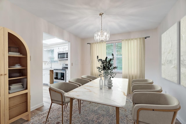 dining space with sink, light hardwood / wood-style floors, and a notable chandelier