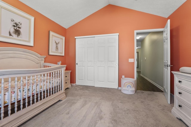 bedroom featuring a crib, light carpet, vaulted ceiling, and a closet