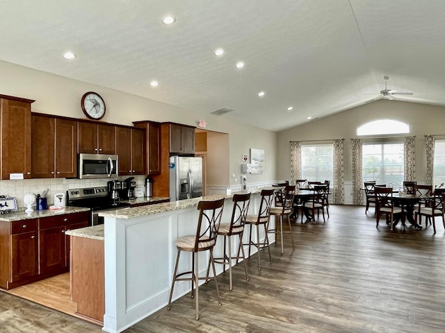 kitchen featuring light stone countertops, stainless steel appliances, ceiling fan, light hardwood / wood-style flooring, and a center island