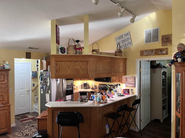 kitchen featuring stainless steel appliances, a kitchen breakfast bar, dark hardwood / wood-style flooring, kitchen peninsula, and track lighting