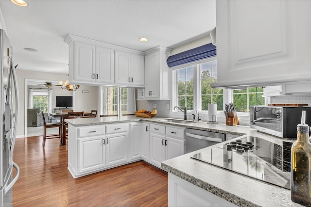 kitchen featuring kitchen peninsula, appliances with stainless steel finishes, white cabinetry, and hardwood / wood-style floors