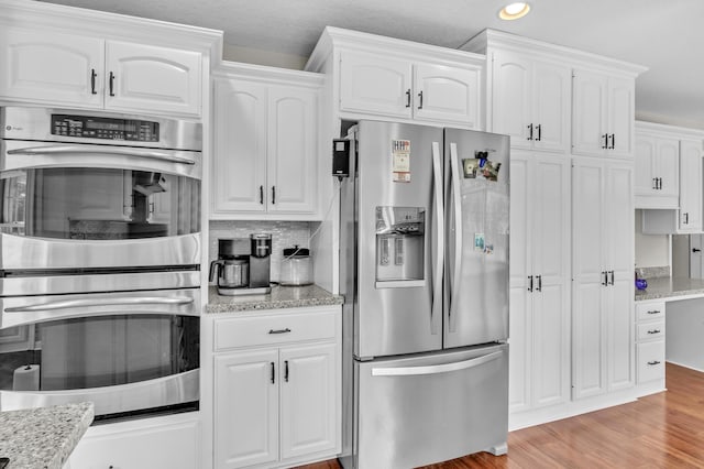 kitchen featuring decorative backsplash, light stone counters, stainless steel appliances, light hardwood / wood-style flooring, and white cabinetry