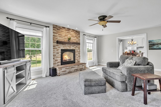 living room with ceiling fan with notable chandelier, light colored carpet, and a brick fireplace