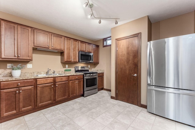 kitchen with light stone countertops, rail lighting, a textured ceiling, stainless steel appliances, and sink