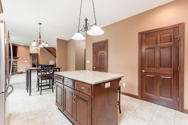 kitchen with light stone countertops, stainless steel fridge, pendant lighting, a fireplace, and a kitchen island