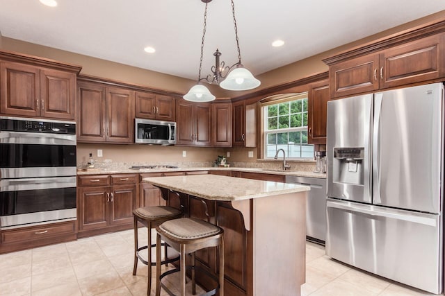 kitchen with light stone countertops, appliances with stainless steel finishes, sink, decorative light fixtures, and a center island