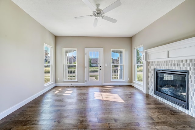 unfurnished living room featuring a glass covered fireplace, dark wood-style flooring, ceiling fan, and baseboards