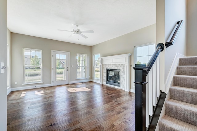 unfurnished living room with baseboards, a ceiling fan, a glass covered fireplace, wood finished floors, and stairs