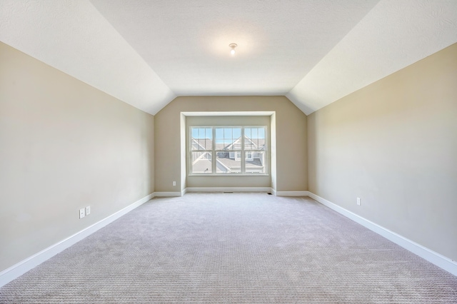 bonus room featuring lofted ceiling, baseboards, a textured ceiling, and light colored carpet