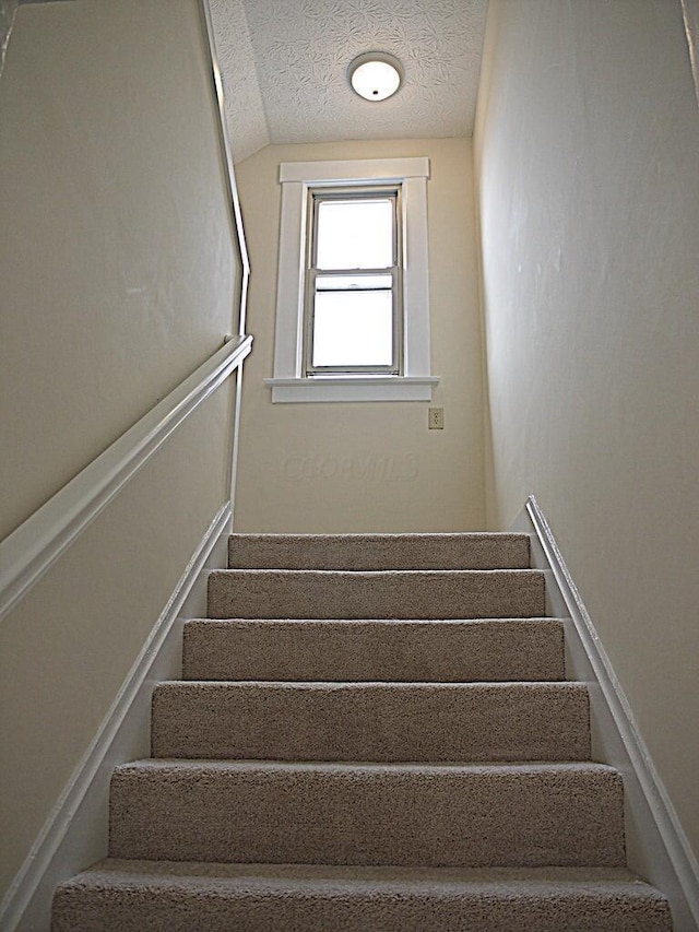 staircase featuring a textured ceiling and vaulted ceiling