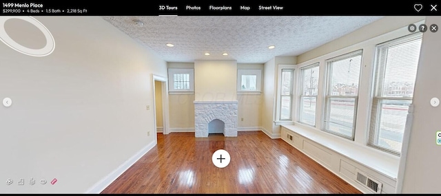 unfurnished living room featuring a fireplace, a textured ceiling, light hardwood / wood-style floors, and a wealth of natural light