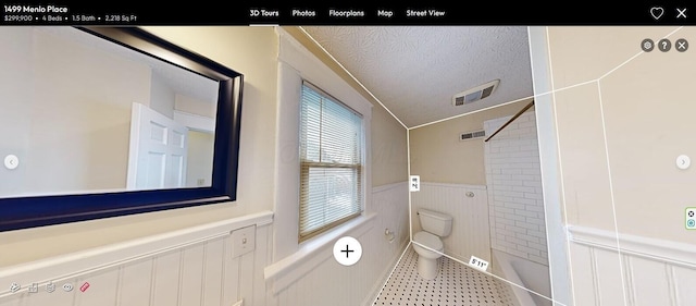 bathroom featuring toilet, a tile shower, tile patterned flooring, and a textured ceiling