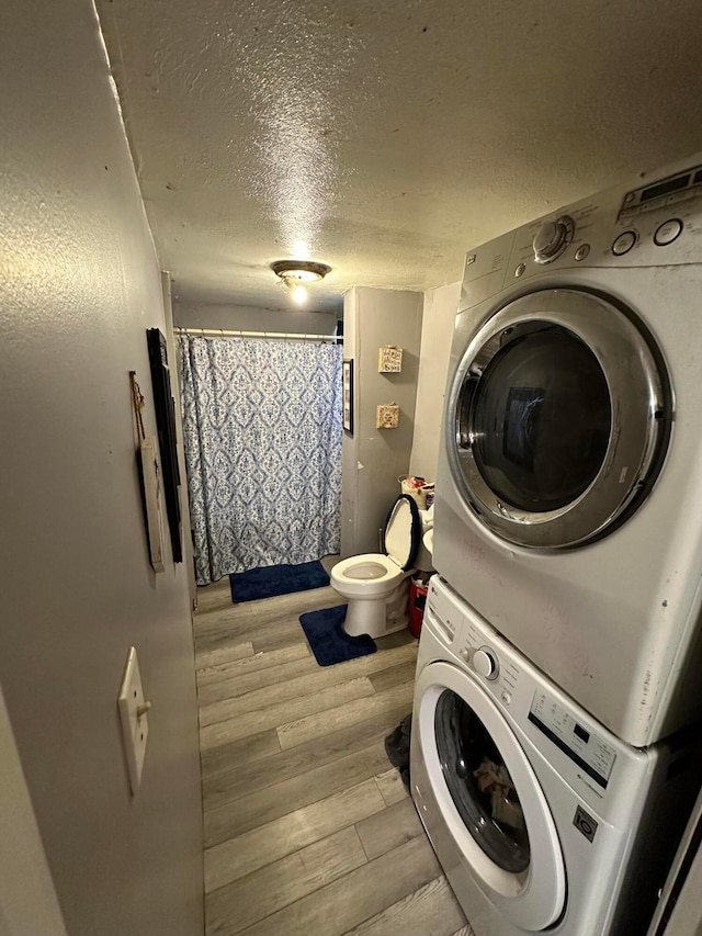 laundry room with stacked washer and dryer, a textured ceiling, and light wood-type flooring