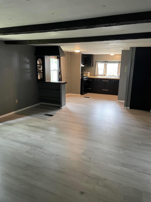 unfurnished living room with beam ceiling, a wealth of natural light, and light hardwood / wood-style floors